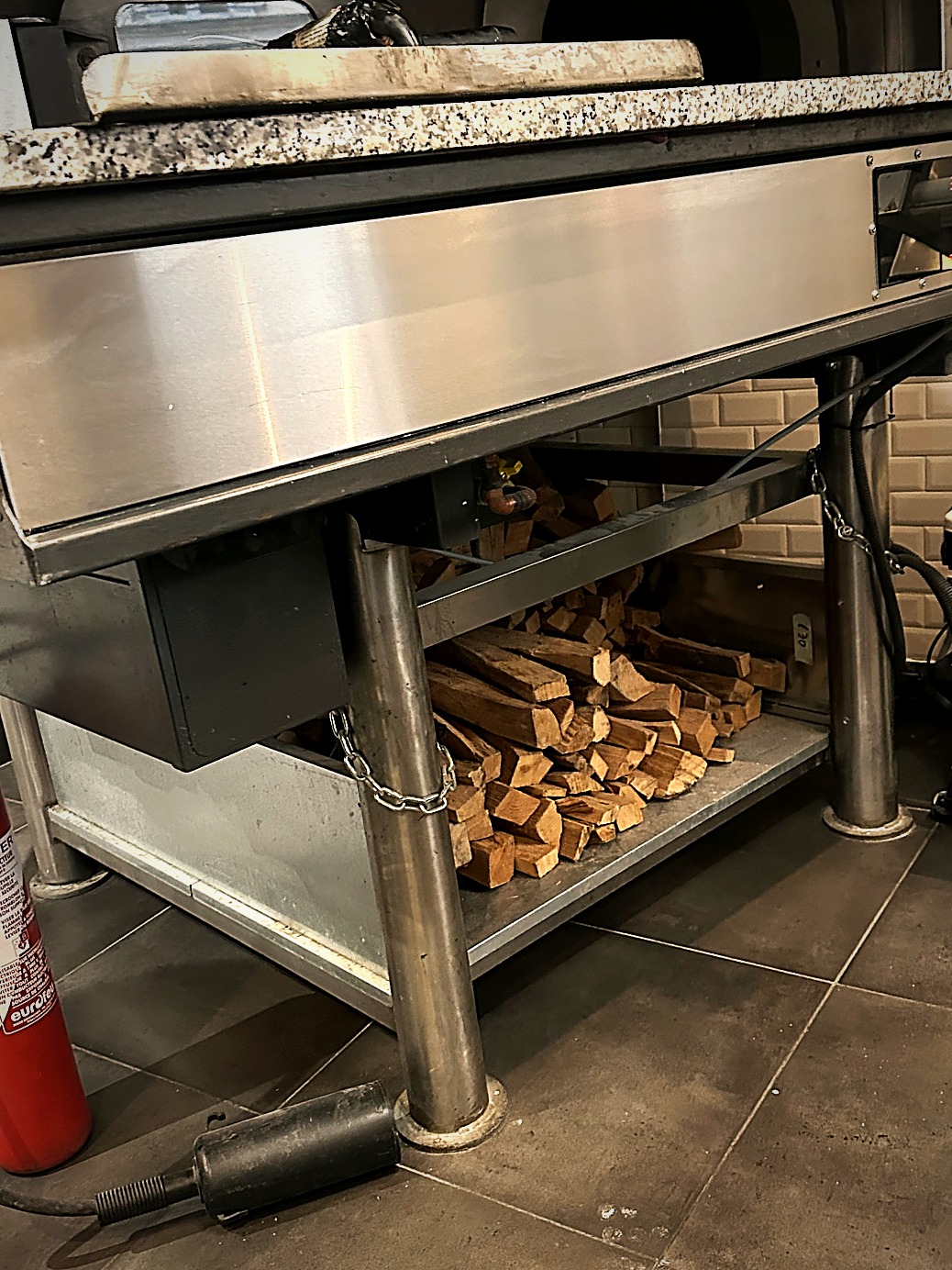 Réserve de bûches rangées sous le four à bois du restaurant ZAMA